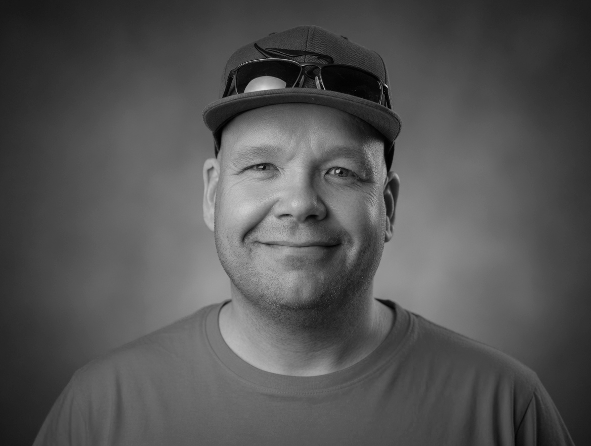 Robert Wennberg, author of The Linn Saga, wearing a vintage SpaceX Falcon 9 cap. Black and white portrait with a warm smile.